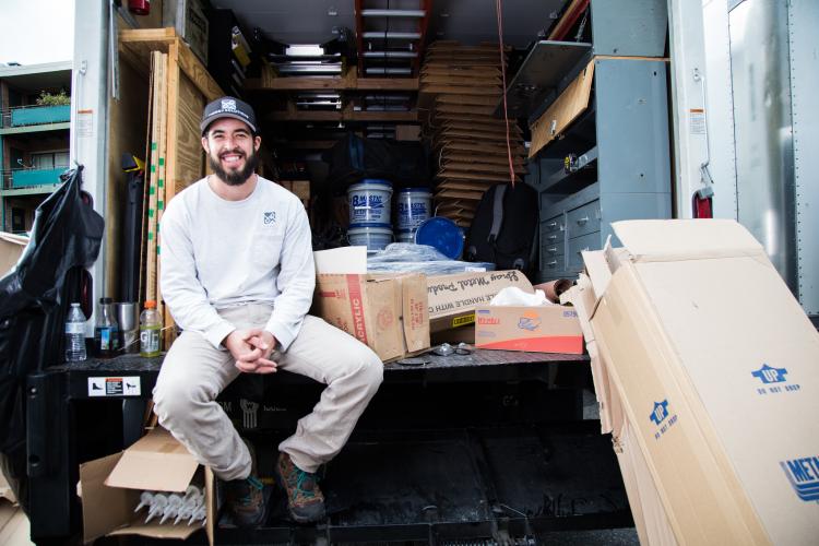 A weatherization worker smiles sitting in the back of a boxtruck.